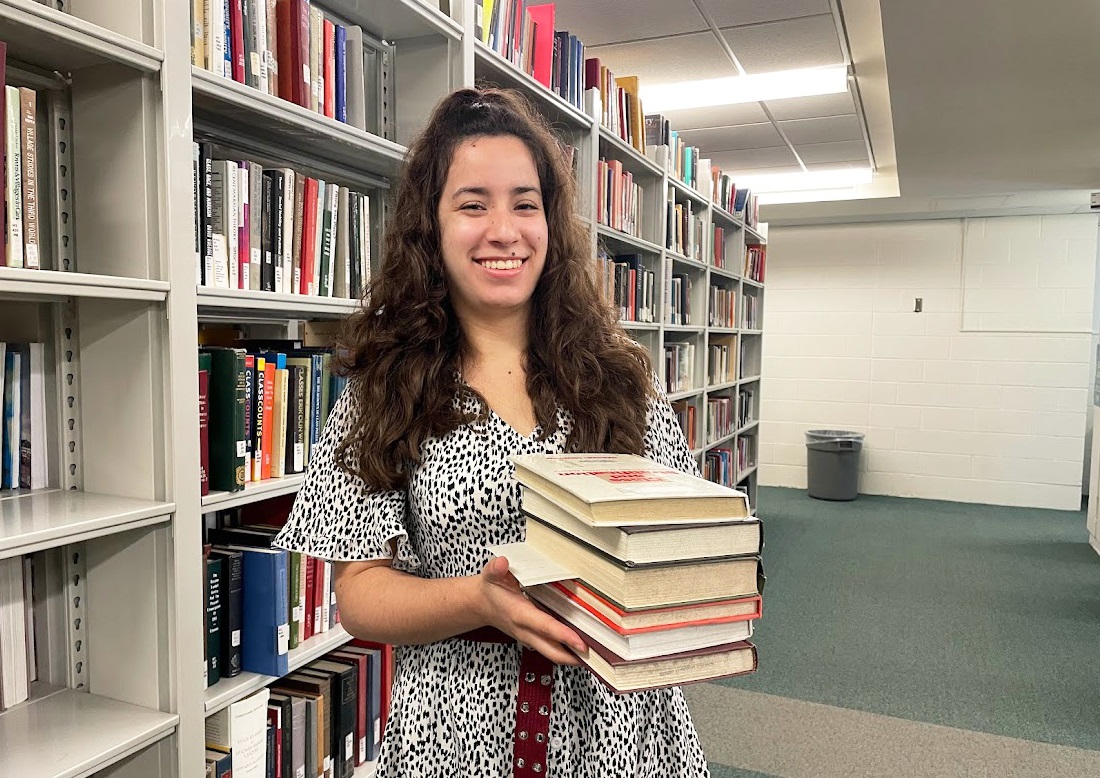 Veronica Larrazabal Zea, library ambassador, can be seen carrying a stack of books at Mills Memorial Library. 