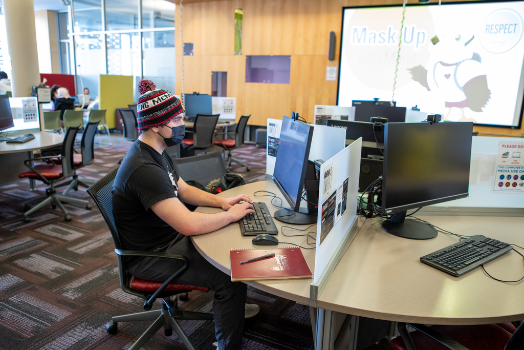 Student using media editing software on computer in Lyons New Media Centre can be seen.