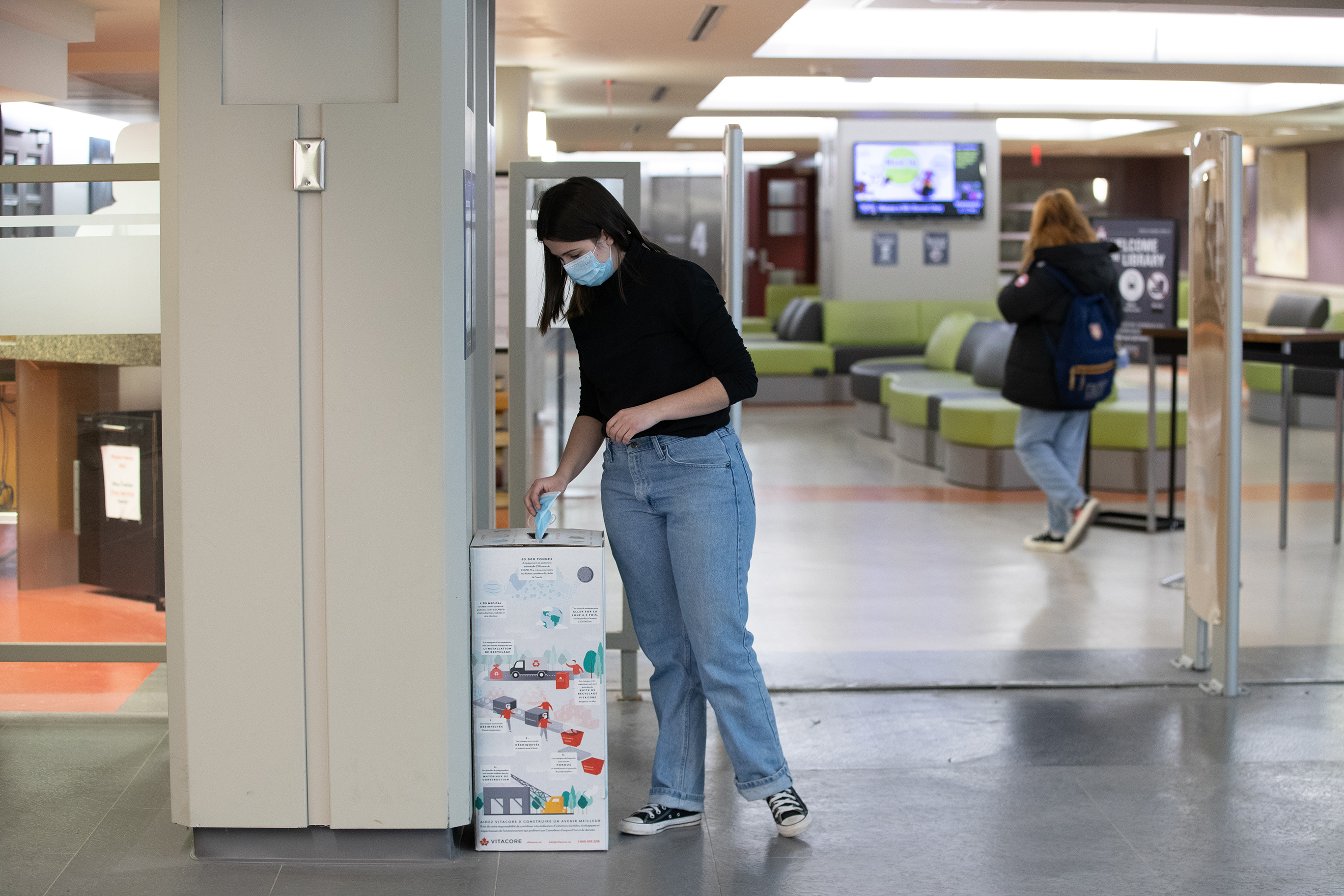 Student placing disposable masks in bin inside Mills Memorial Library can be seen.