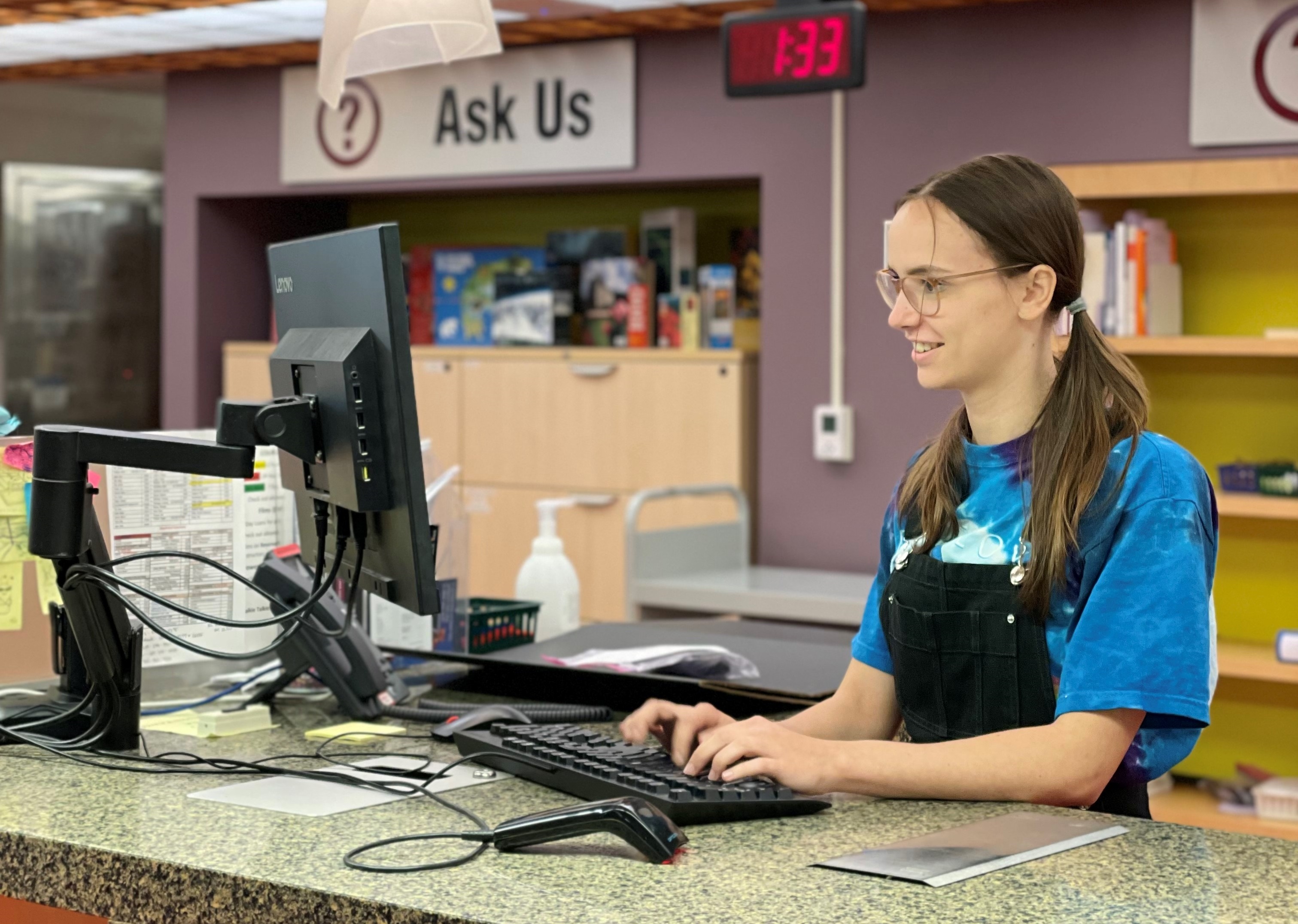 Library student assistant working at Mills service desk can be seen.