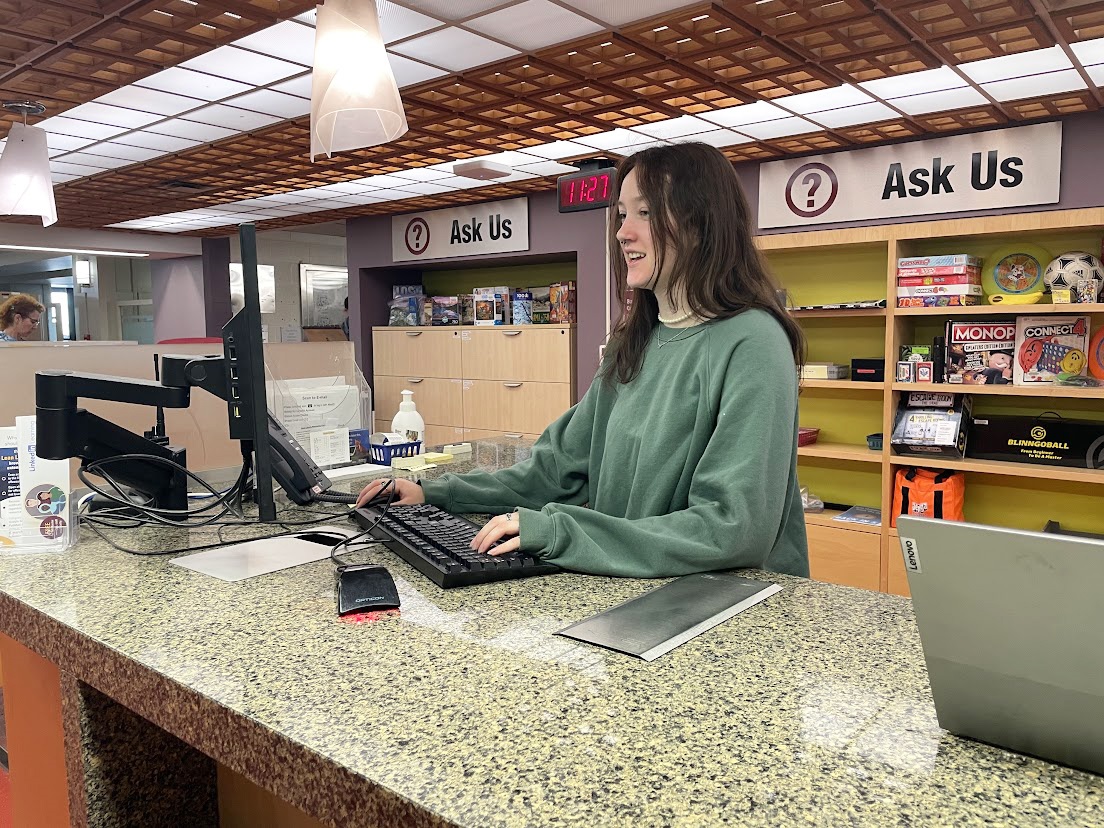 Clara Rakovac, student assistant, can be seen working at the service desk in Mills Memorial Library.