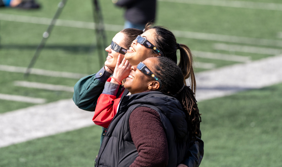 Three McMaster community members look up at the sky wearing their solar eclipse glasses. 