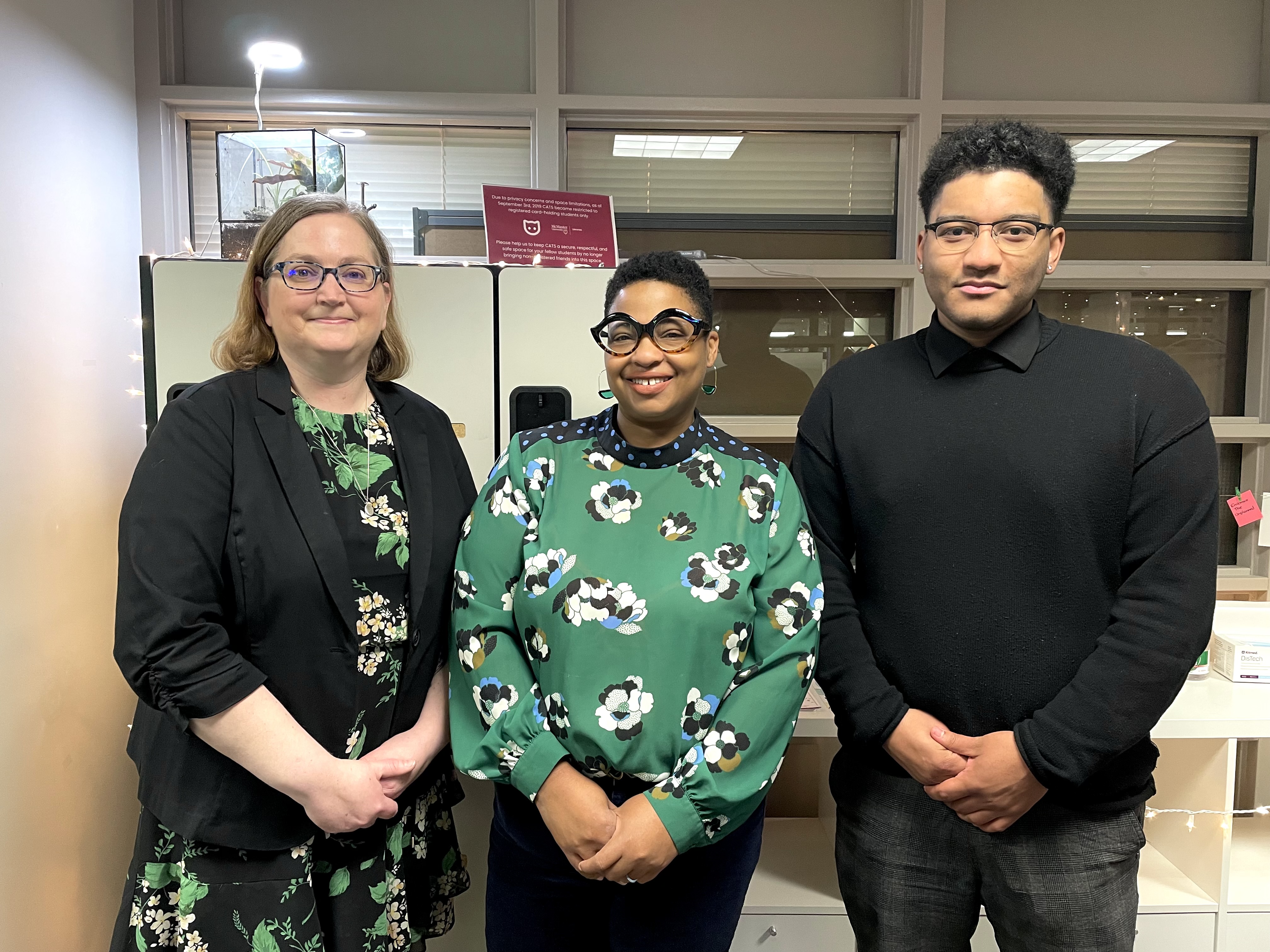 Nancy Waite with long blonde hair, glasses and a black blazer, Crystal Kerr with short black hair, glasses and a green shirt, and Miles Riel-Walker with short black hair, glasses and a black shirt stand together in the Campus Accessible Tech Space.