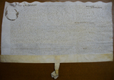 Handwritten vellum document with seal tag at bottom and scalloped edge at top