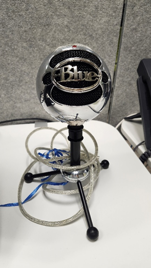 A Snowball microphone with its cable coiled around the base, placed on a white desk