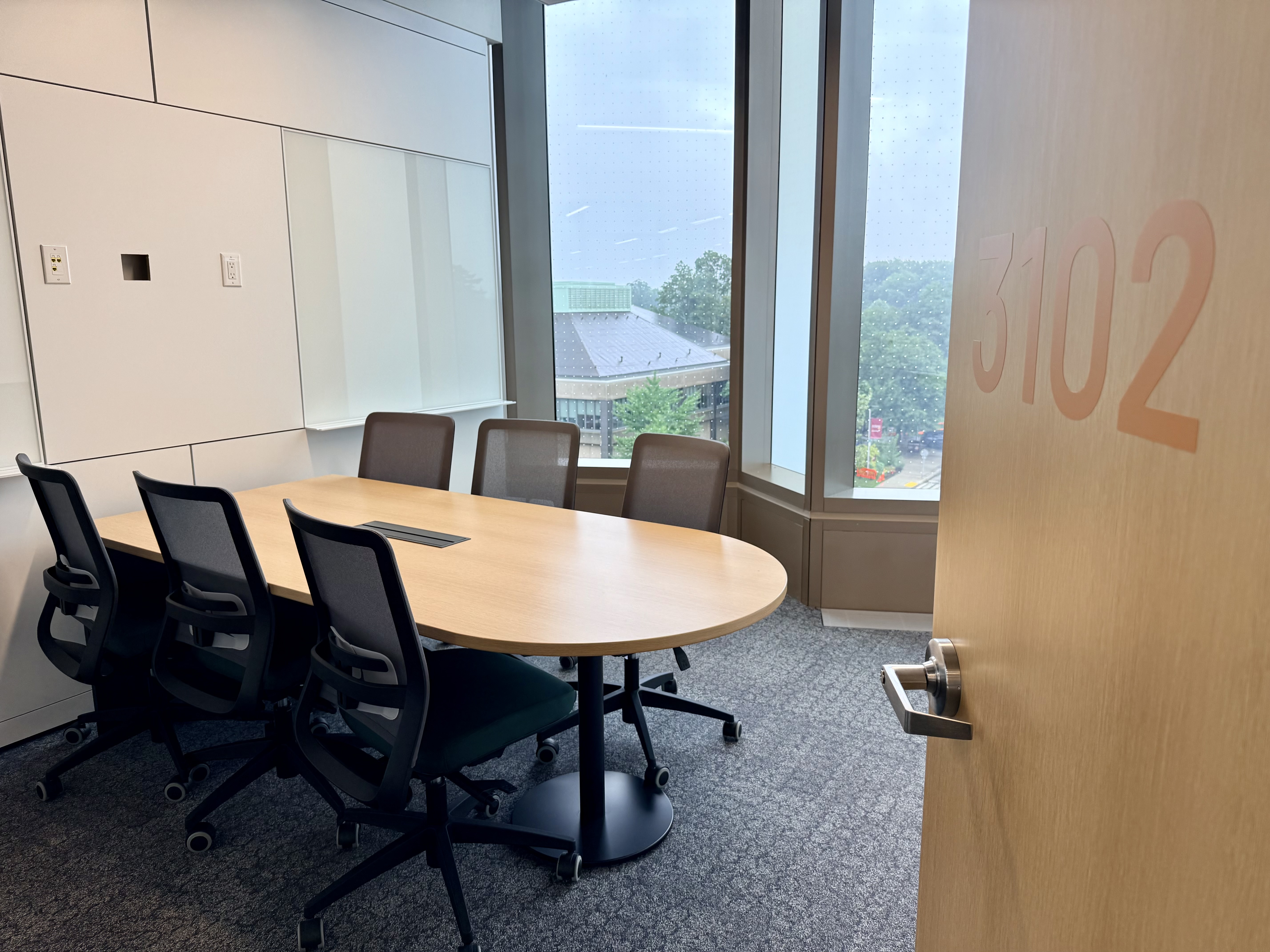 A group study room in Innis Library lined with windows featuring a table with 6 chairs around a wood-topped table.