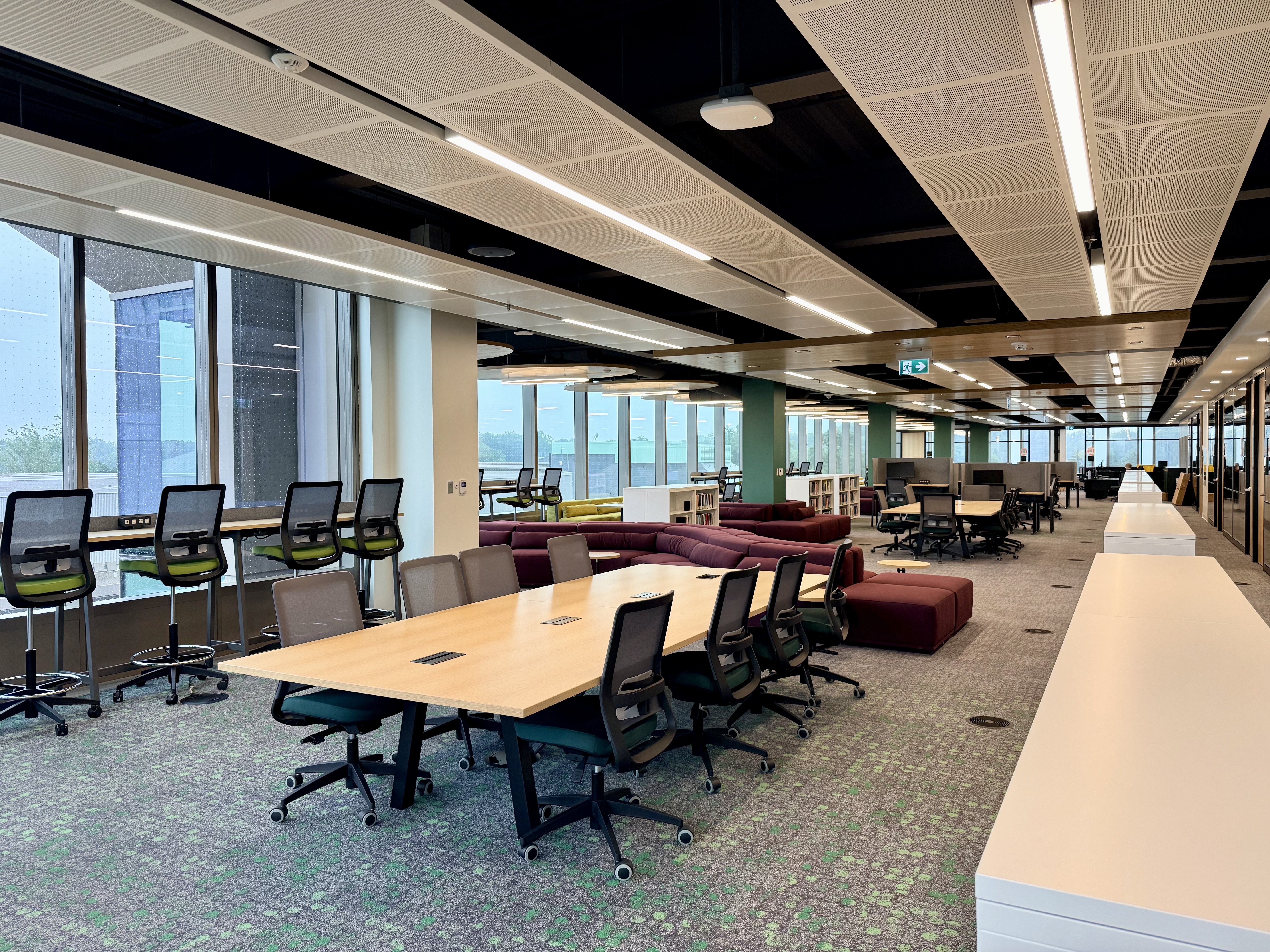 Innis Library study area with bookstacks, tables, chairs, lounge seating, and large windows overlooking the campus.