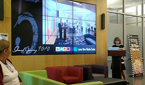 Vivian Lewis speaking at a podium next to the video wall in Lyons New Media Centre.